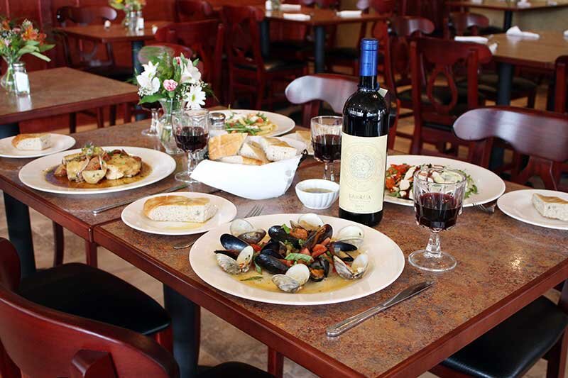 Dining room table with multiple entrees with wine bottle and glasses